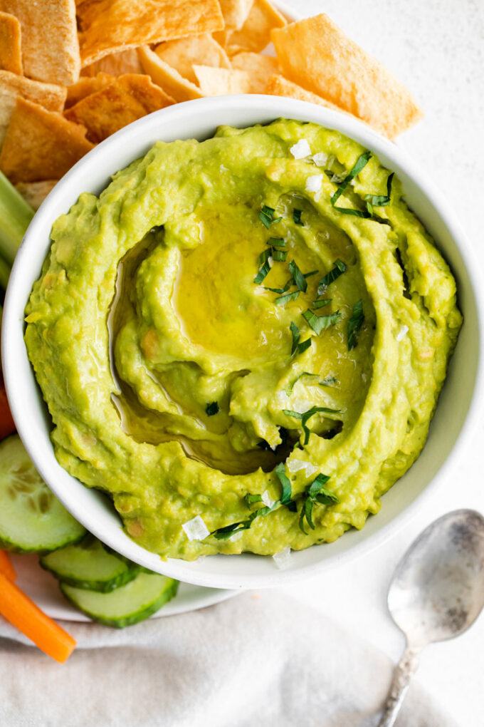 white bowl filled with green avocado hummus and surrounded by chips and veggies