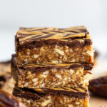 date and nut bars topped with chocolate and peanut butter drizzle. 3 bars stacked on top of each other