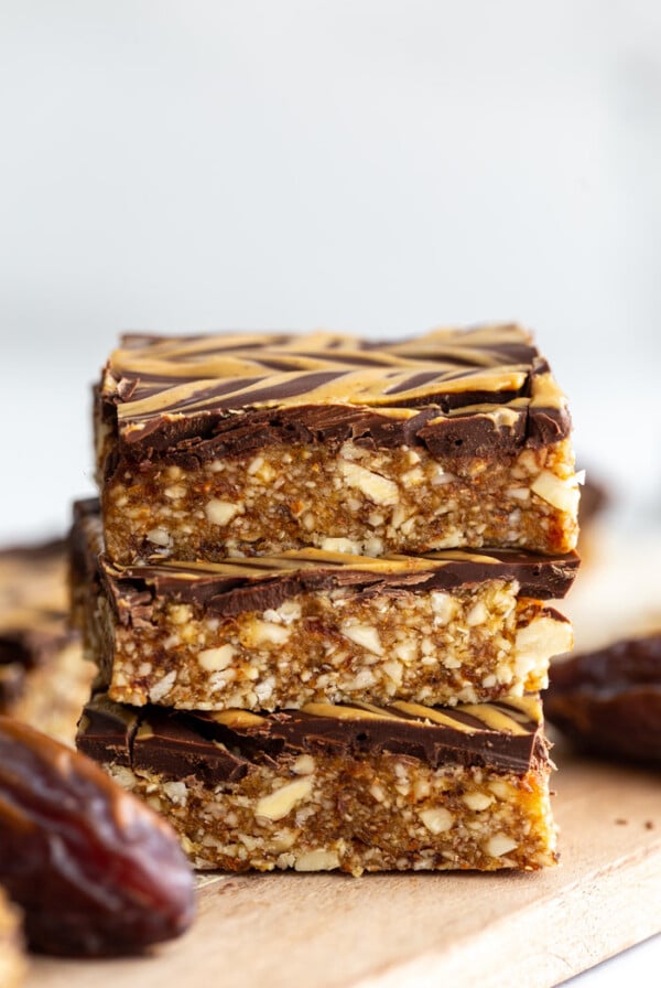 date and nut bars topped with chocolate and peanut butter drizzle. 3 bars stacked on top of each other