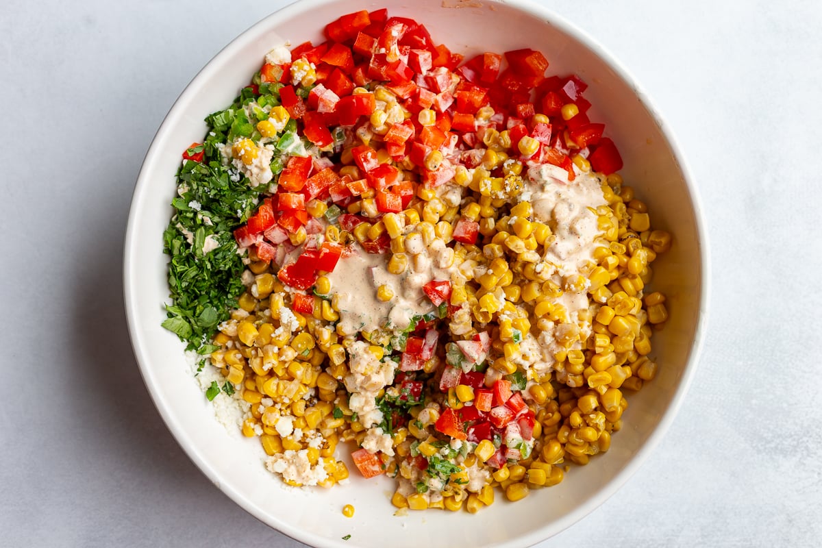 mexican street corn salad in a large white bowl before it's all been mixed together