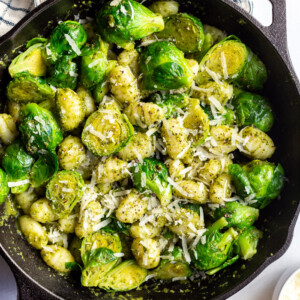black cast iron skillet filled with gnocchi and brussels sprouts in a pesto sauce and topped with with fresh cheese