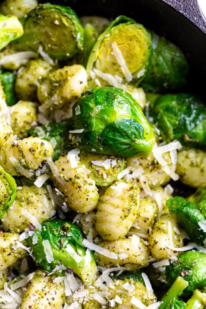 black cast iron skillet filled with gnocchi and brussels sprouts in a pesto sauce and topped with with fresh cheese