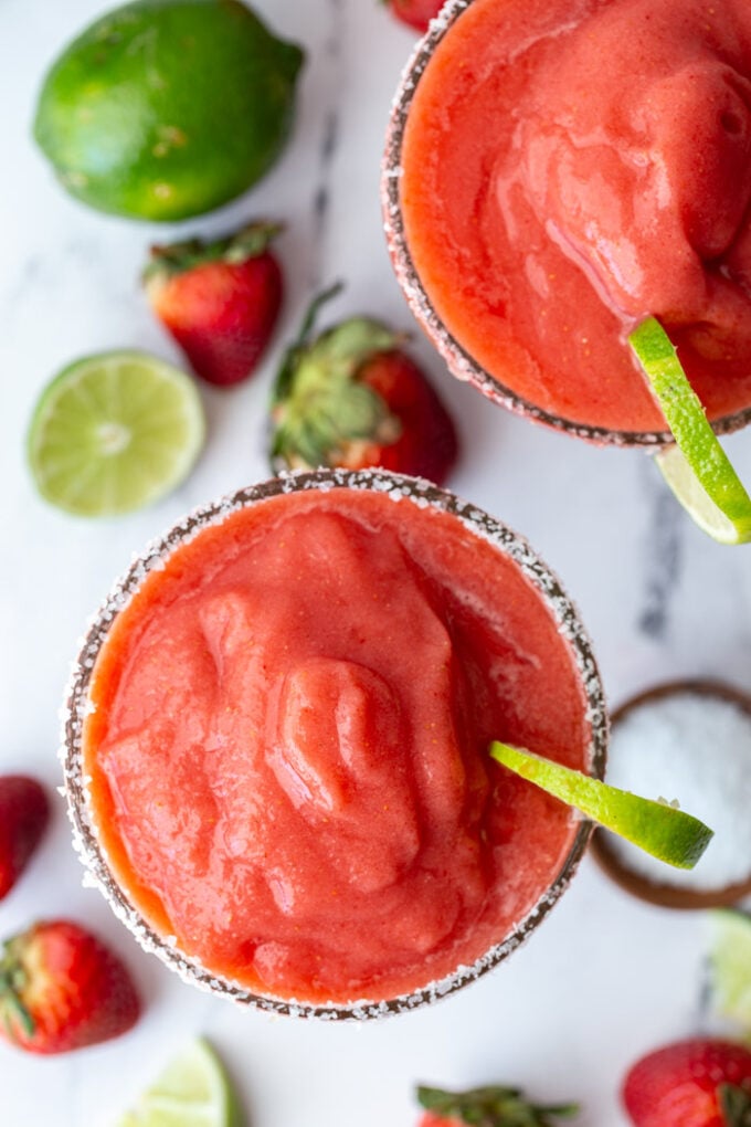 top down shot of 2 frozen strawberry margaritas with fresh limes and strawberries in the scene