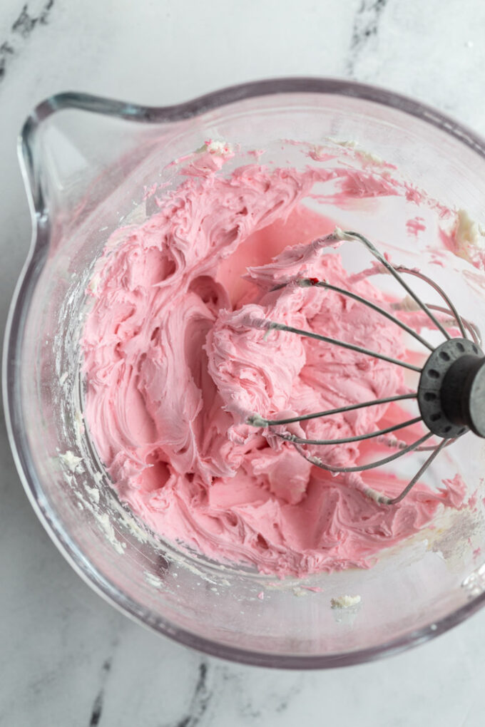 light pink buttercream cookie frosting in the base of a stand mixer with the whisk attachment sitting in the bowl