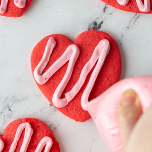 red heart cookie being frosted with pink frosting