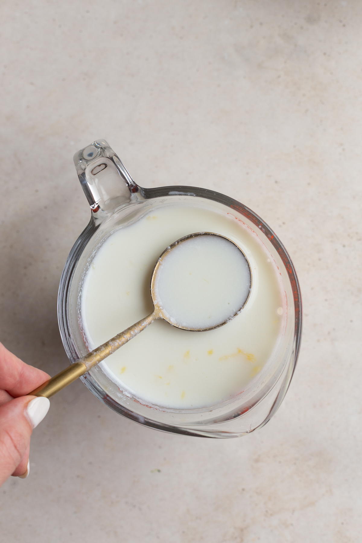 Using a spoon to stir milk and lemon juice in a spouted measuring glass.