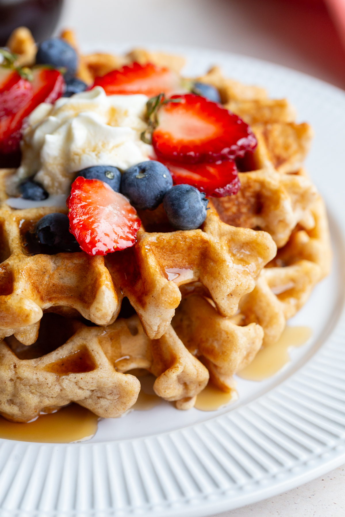 Waffle on a white plate topped with berries and whipped cream.