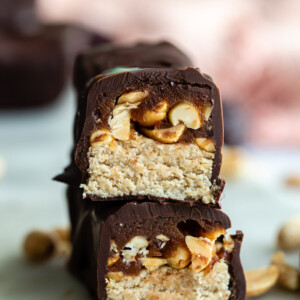 homemade snickers candy bar cut in half and stacked up so that you can see the inside of it. more bars in the background