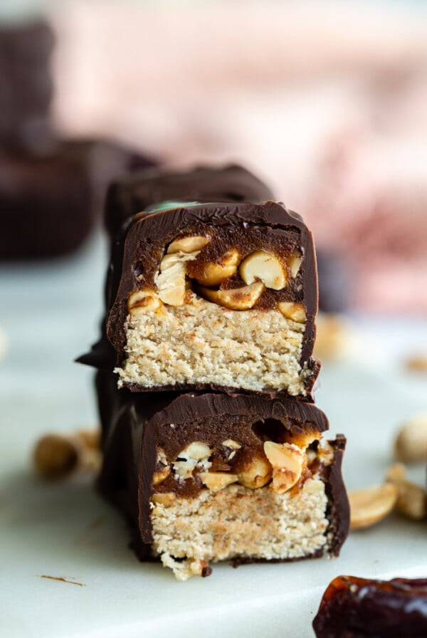 homemade snickers candy bar cut in half and stacked up so that you can see the inside of it. more bars in the background