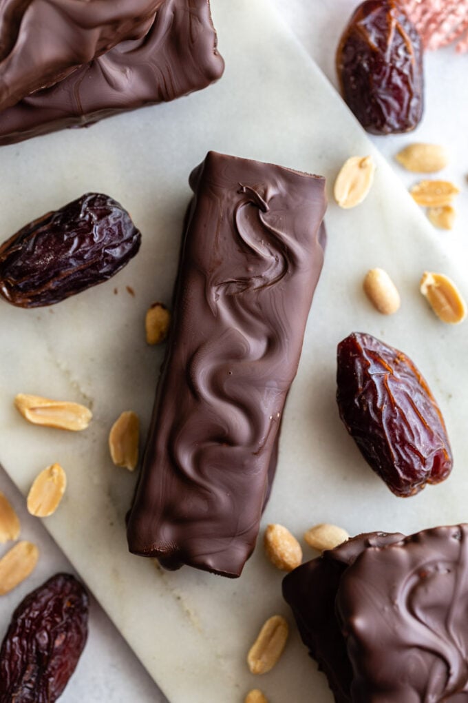 top down shot of a homemade snickers bars surrounded by peanuts and dates