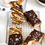 healthy granola bars drizzled with chocolate and sprinkled with sea salt and hand holding one up