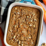 green casserole dish filled with baked carrot cake oatmeal. carrots and a towel on the side
