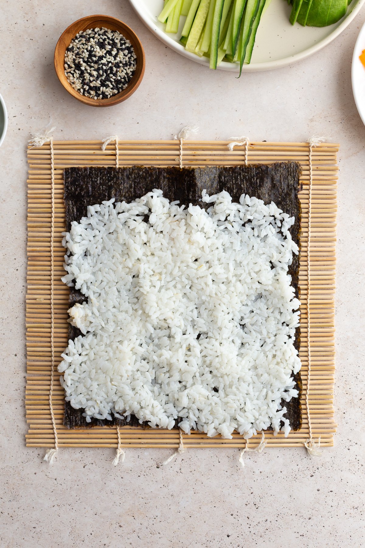 Topping a nori sheet that is on a sushi mat with rice.