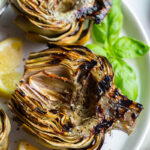 Grilled artichokes on a plate with lemon wedges.