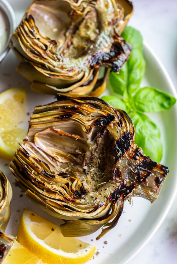Grilled artichokes on a plate with lemon wedges.