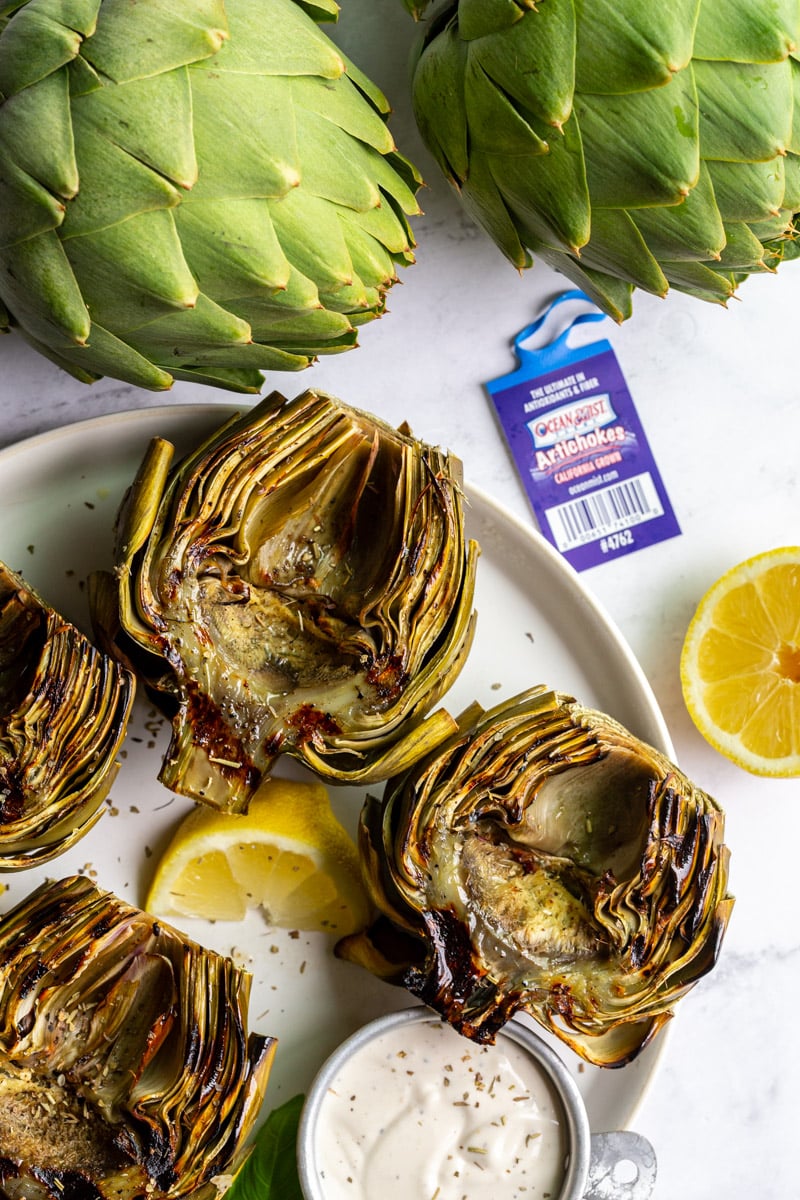 large plate with grilled artichokes on it as well as fresh basil and lemon slices
