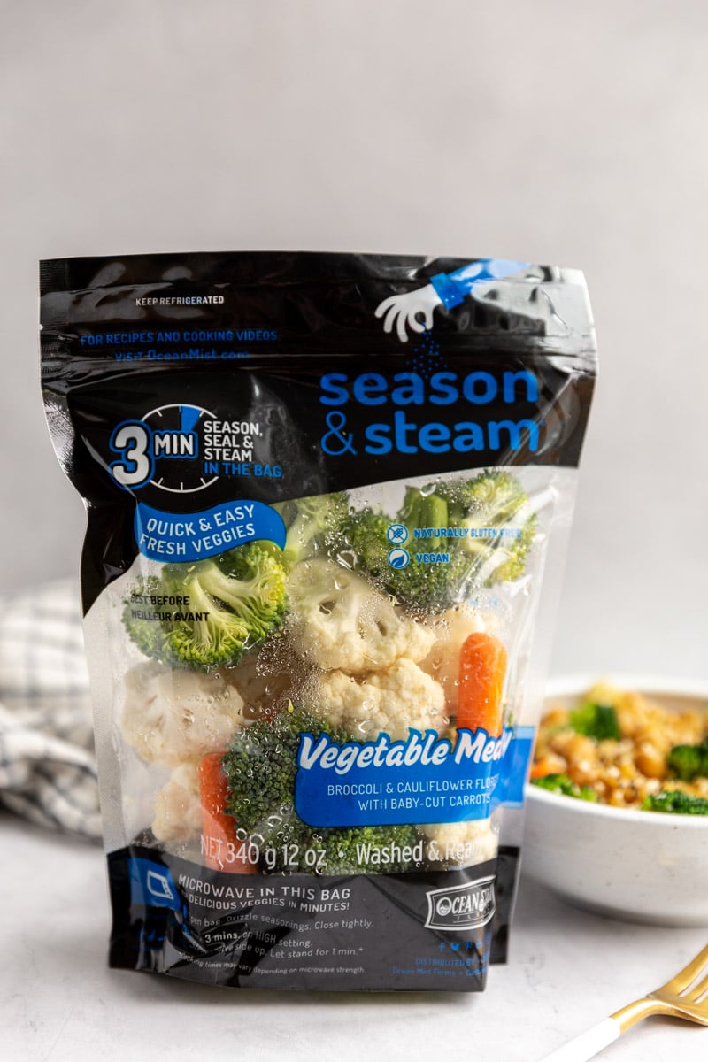 bag of ocean mist season and steam vegetable medley standing up on a table with a bowl of veggie ramen behind it