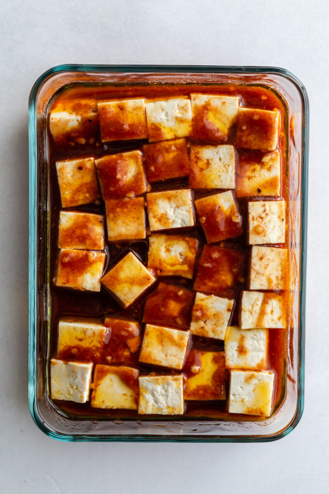 glass dish filled with tofu cubes that are covered in a dark colored marinade