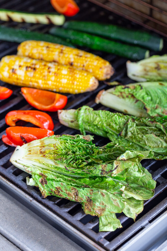 fresh veggies cooking on a grill including romaine lettuce, red bell pepper, corn, and zucchini