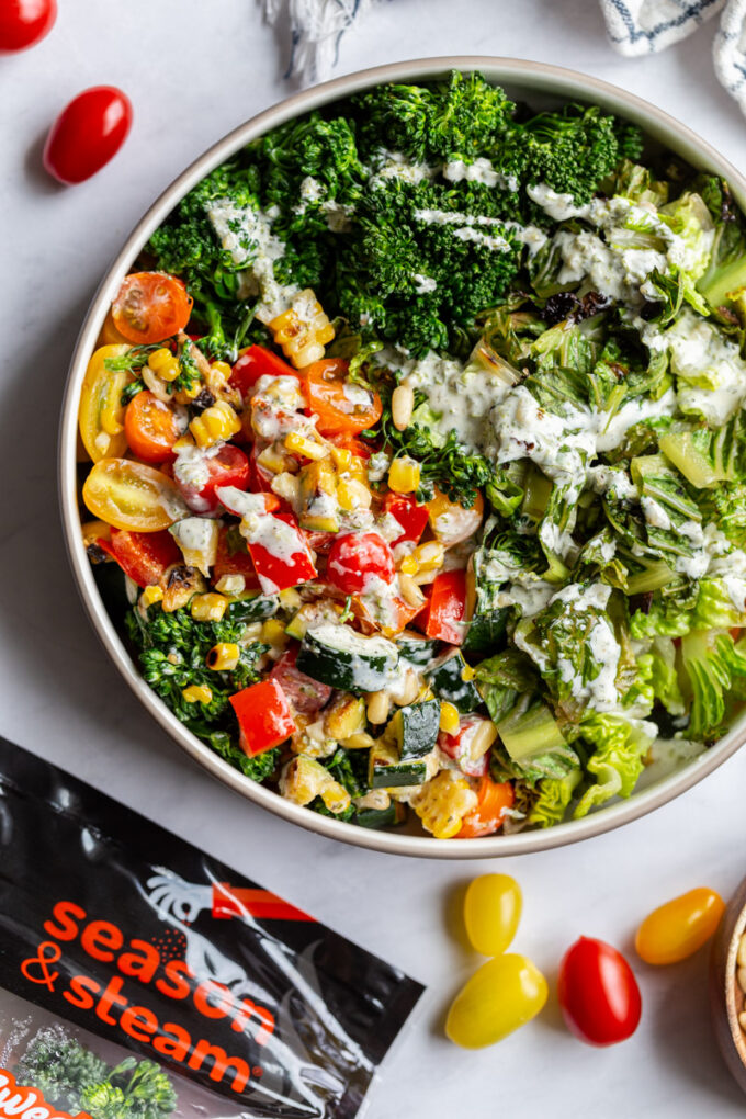 large salad in a bowl with a package of season and steam veggies in the corner