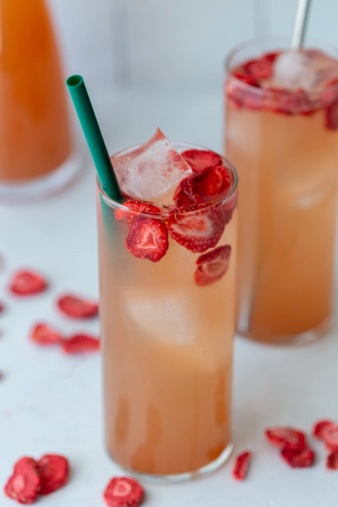 tall glass filled with a pink drink, ice, and strawberries