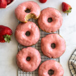 strawberry glazed donuts on a wire cooling rack with fresh strawberries around
