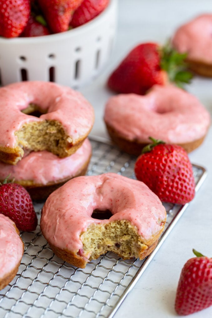 baked donuts topped with a pink strawberry glaze. big bite take out of the front donut