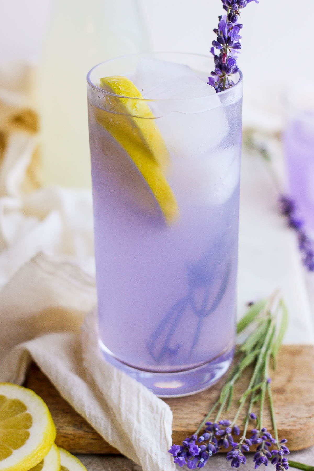 lavender lemonade in a tall glass with ice and fresh lavender plus lemon slices in the glass