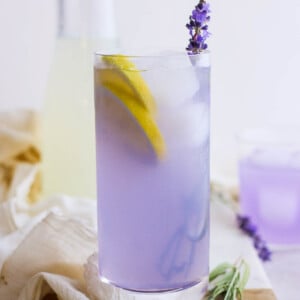 lavender lemonade in a tall glass with ice and fresh lavender plus lemon slices in the glass