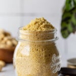 vegan parmesan cheese in a glass jar with cashews in the background