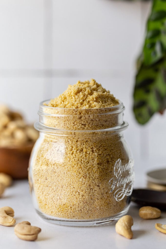 vegan parmesan cheese in a glass jar with cashews in the background