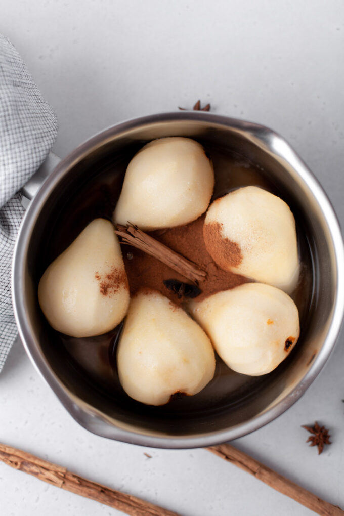 adding pears to a large pot with a cinnamon stick