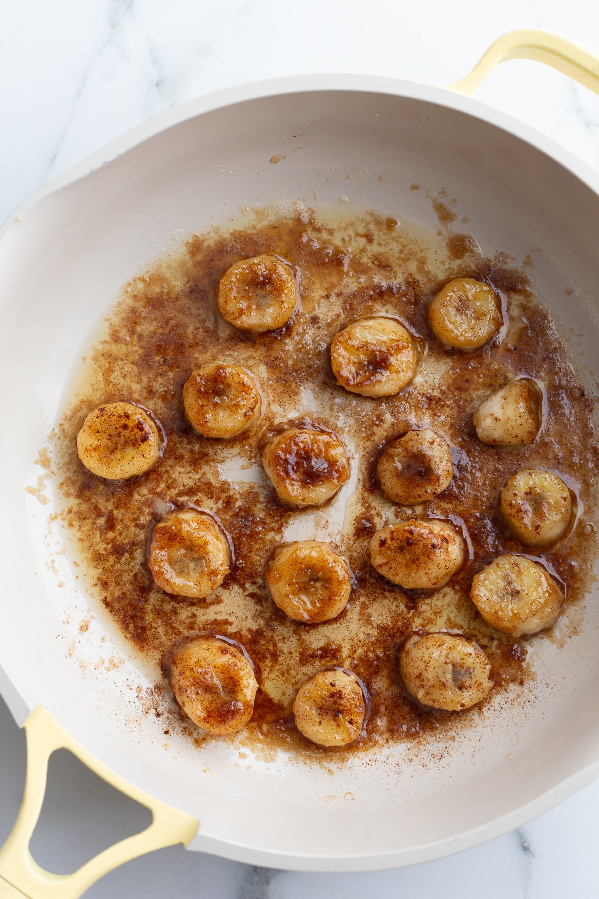 bananas and brown sugar cooking in a yellow skillet to caramelize them