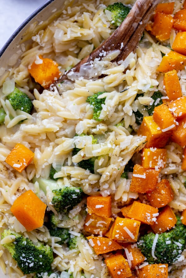 up close shot of cheesy orzo in a skillet with butternut squash and broccoli mixed in