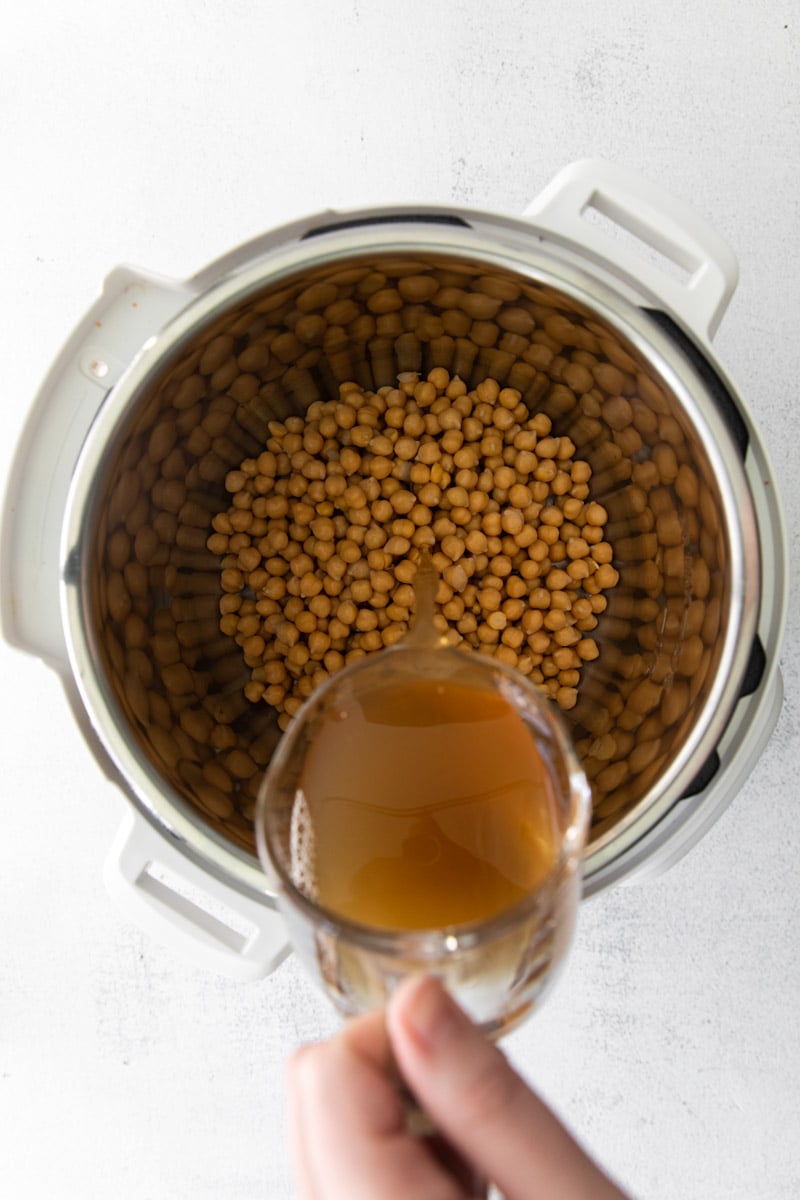 pouring vegetable broth in an Instant Pot with chickpeas