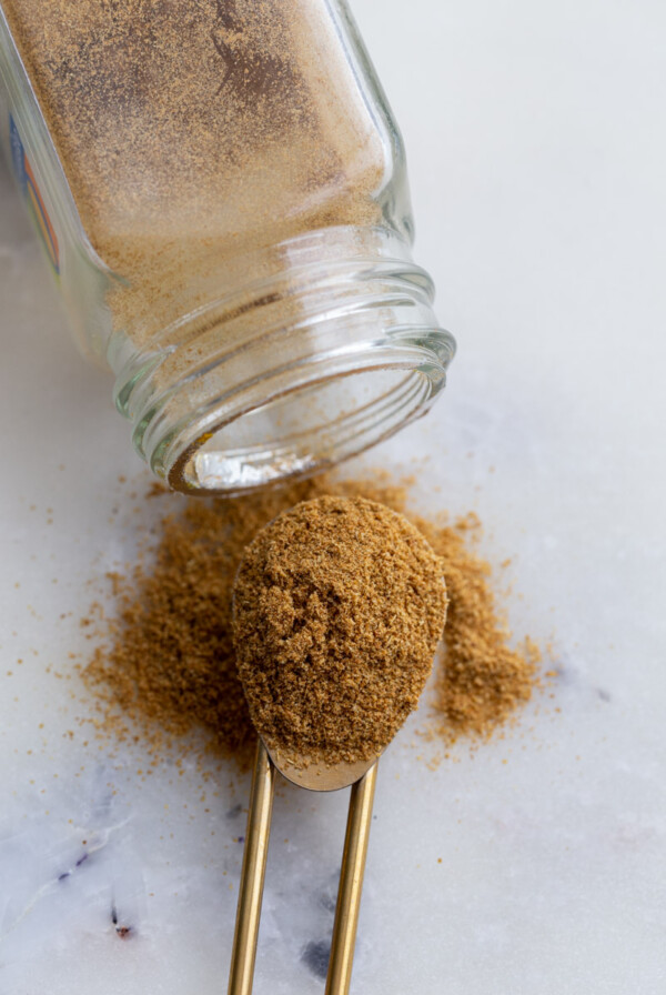 spice jar of cumin spilled out with a scoop of cumin beside it