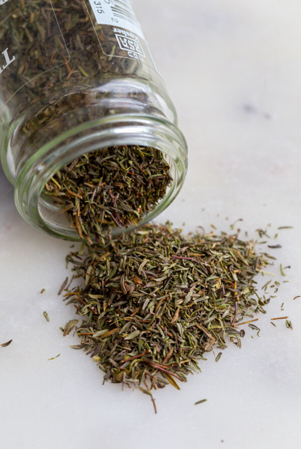 dried thyme spilling out of a glass spice jar
