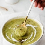 using a spoon to scoop up vegan zucchini soup out of a bowl