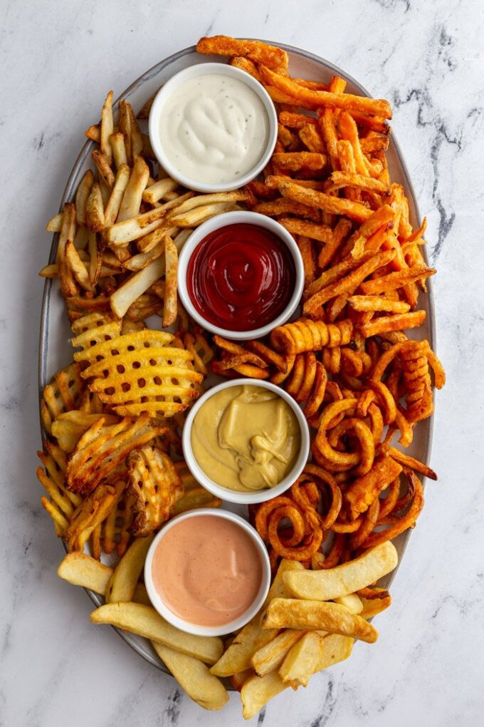 different types of French fries on a plate with dipping sauces