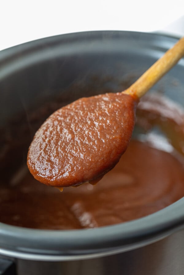 apple butter in a slow cooker with a spoonful being held up to the camera
