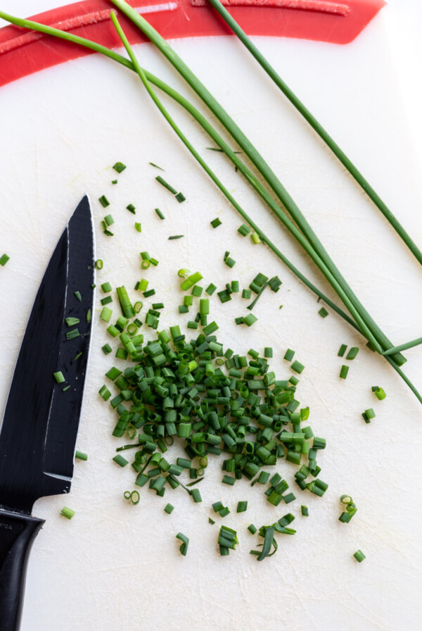 cutting board with a small knife on it next to diced and whole chives