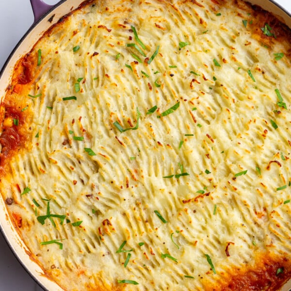 vegan shepherd's pie with crispy potato topping and red liquid that's bubbled out around the edges. The pie is in a large purple skillet