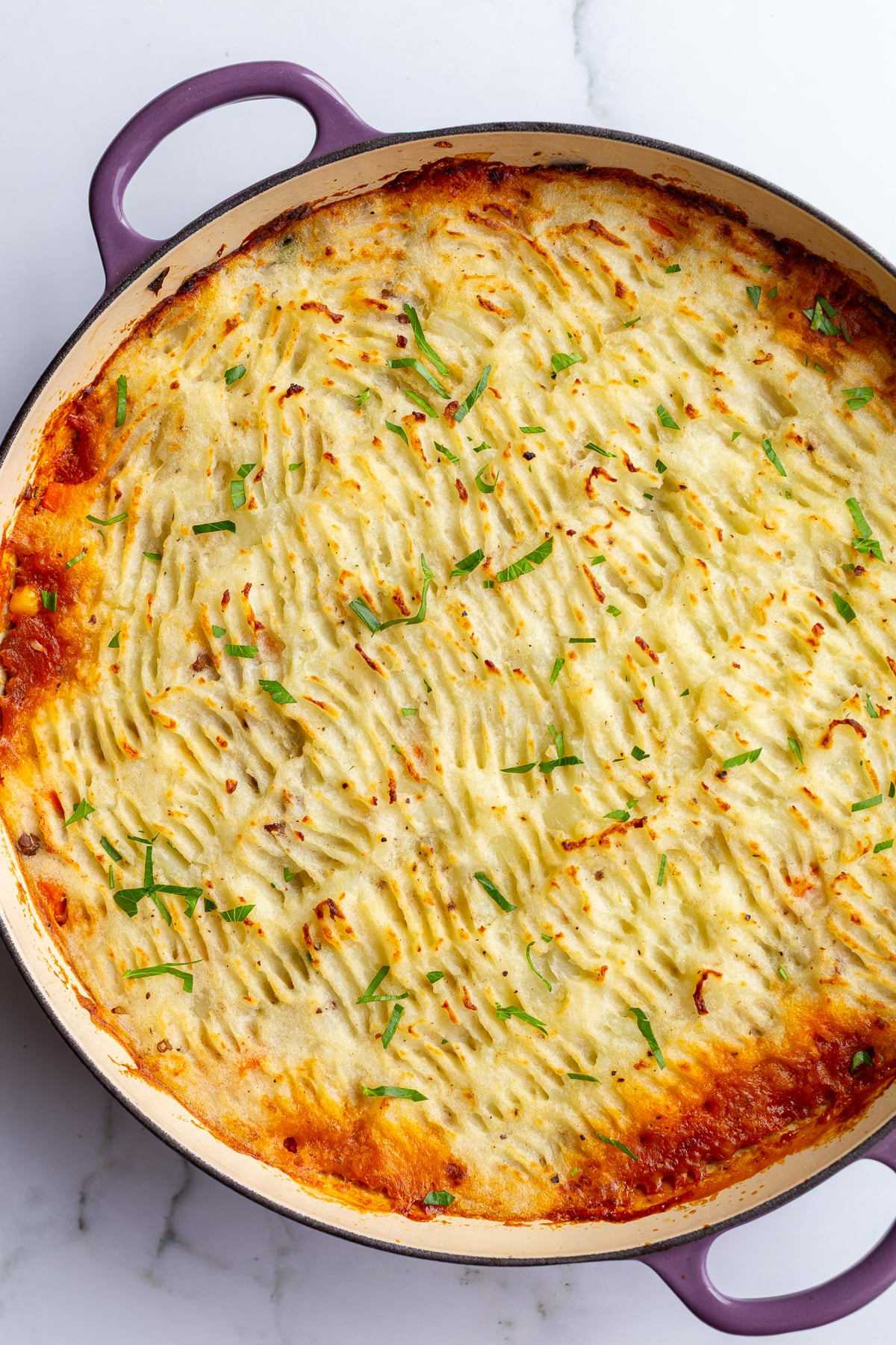 vegan shepherd's pie with crispy potato topping and red liquid that's bubbled out around the edges. The pie is in a large purple skillet