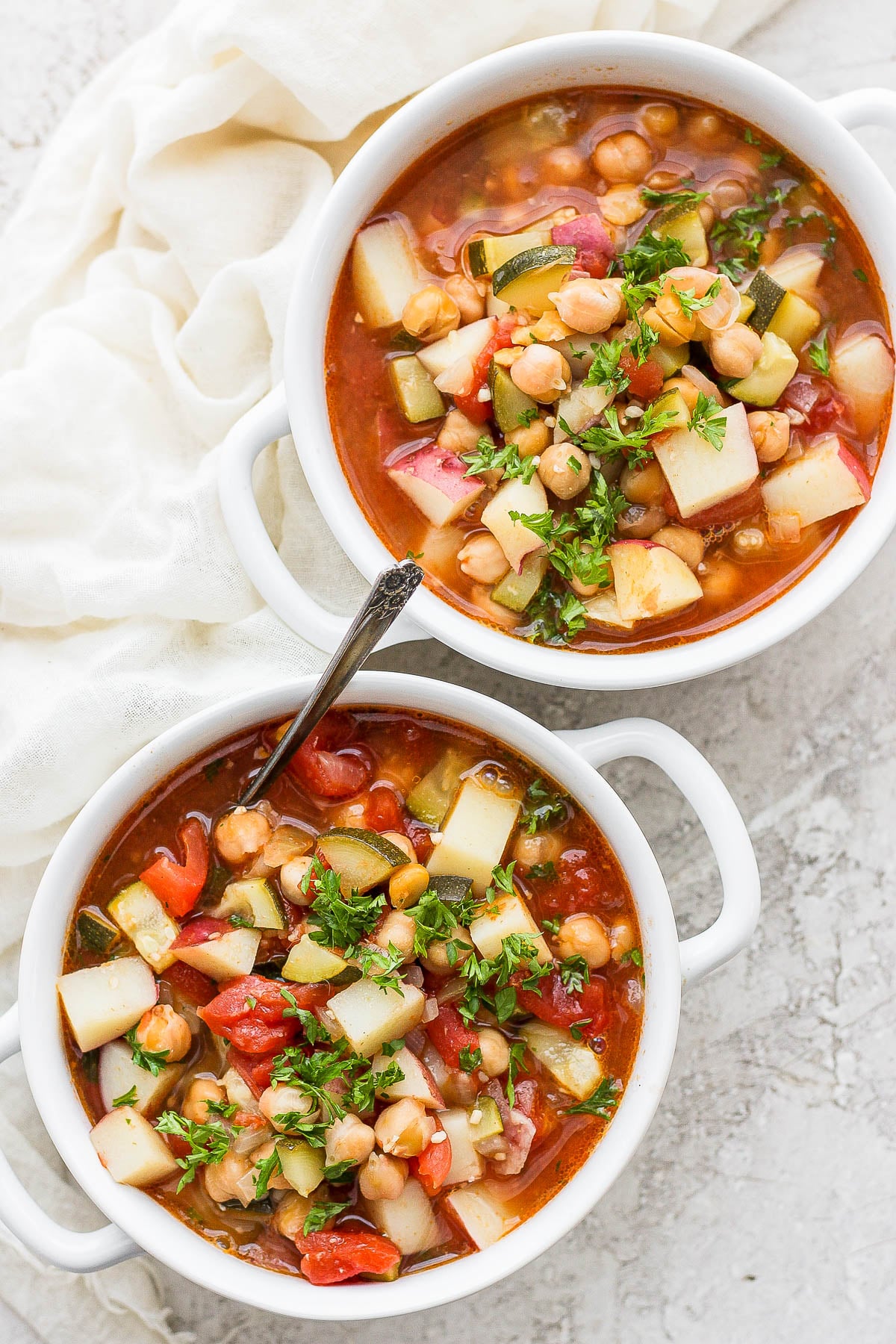 Two bowls of soup with vegetables and chickpeas in a tomato broth.