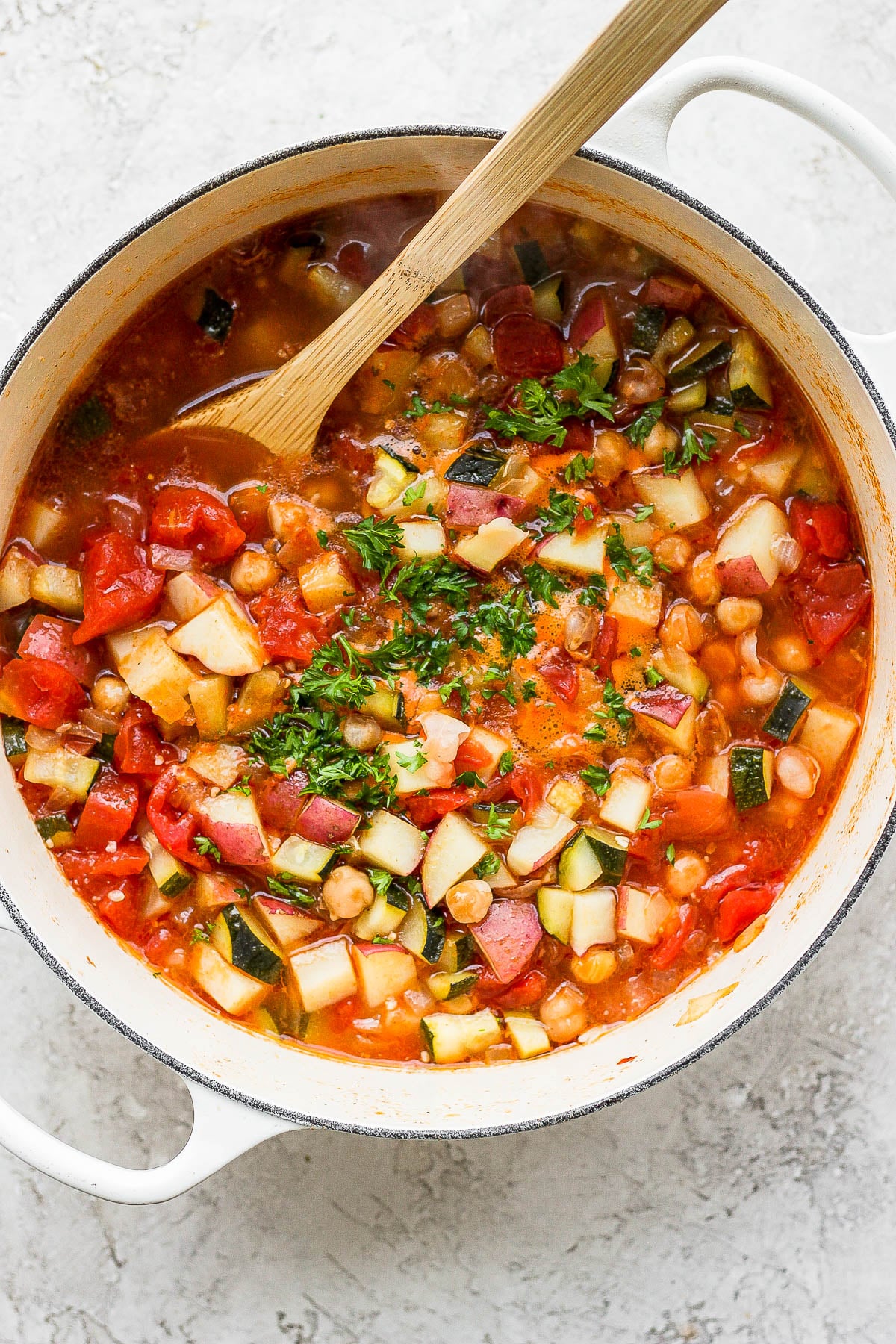 Fresh herbs sprinkled over a vegetable soup in a large pot.
