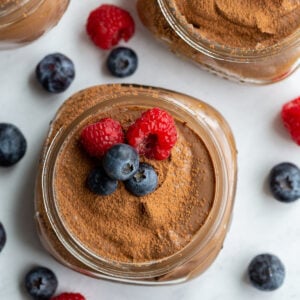 chocolate vegan pudding in a small glass jar topped with blueberries and raspberries