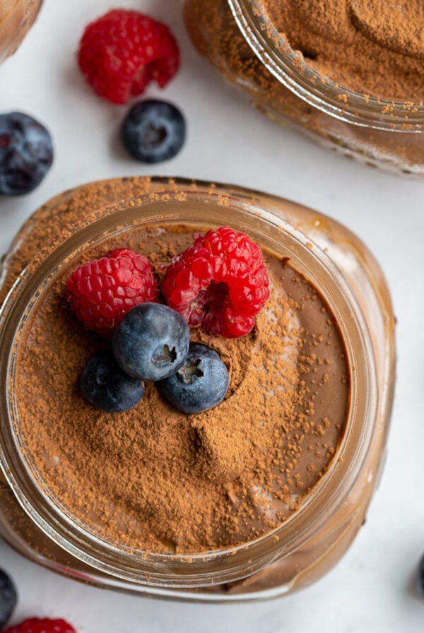 chocolate vegan pudding in a small glass jar topped with blueberries and raspberries