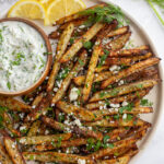 Greek fries on a large plate served with a bowl of dipping sauce