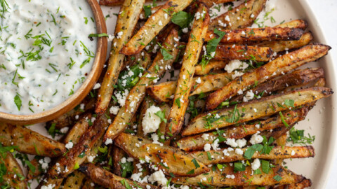 Greek fries on a large plate served with a bowl of dipping sauce