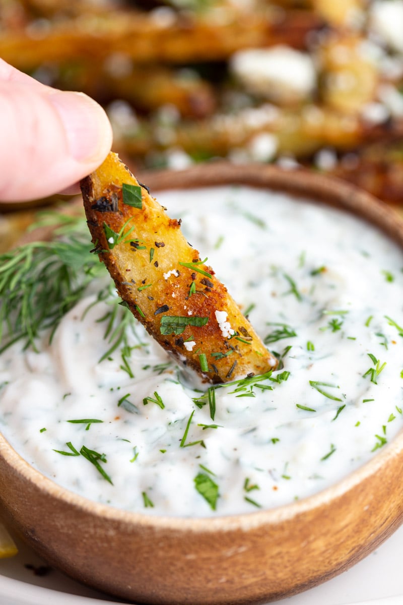 dipping Greek fries into a small bowl of dill sauce
